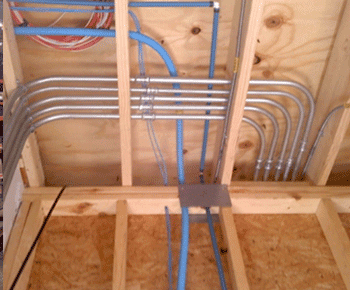 Metal electrical conduit pipes are neatly arranged and bent at right angles, mounted on the wooden framing of a ceiling under construction by a pre-eminent electrical service company in Alamance County, NC. Blue wires are visible running through the conduits.