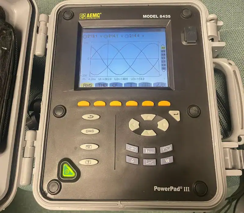 A close-up of an AEMC PowerPad III Model 8435 power quality analyzer displaying waveform graphs and measurement data, as used by a pre-eminent electrical service company in Alamance County, NC. Various buttons and controls are visible.