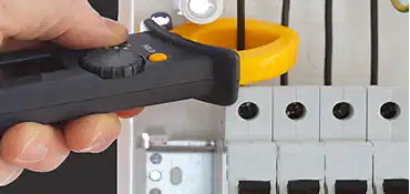 A hand holding a digital clamp meter measures electrical current on wires inside a circuit breaker panel for a pre-eminent electrical service company in Alamance County, NC.