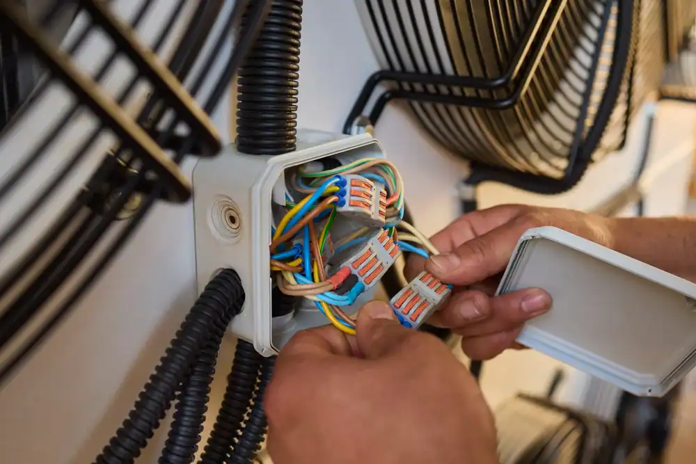 Close-up of hands wiring electrical connections in a junction box, with various colored wires and wire connectors&mdash;showcasing the expertise of a pre-eminent electrical service company in Alamance County, NC.