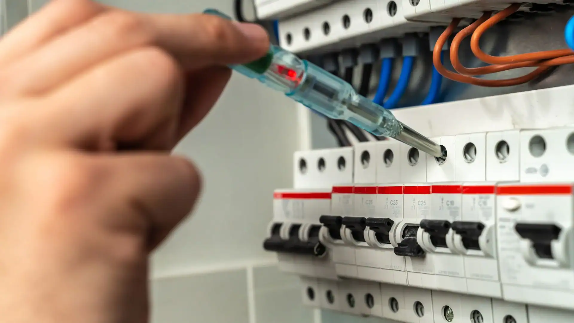 A hand uses a voltage tester screwdriver to check a circuit breaker inside an electrical panel with multiple switches and wires—standard practice for a pre-eminent electrical service company in Alamance County, NC.