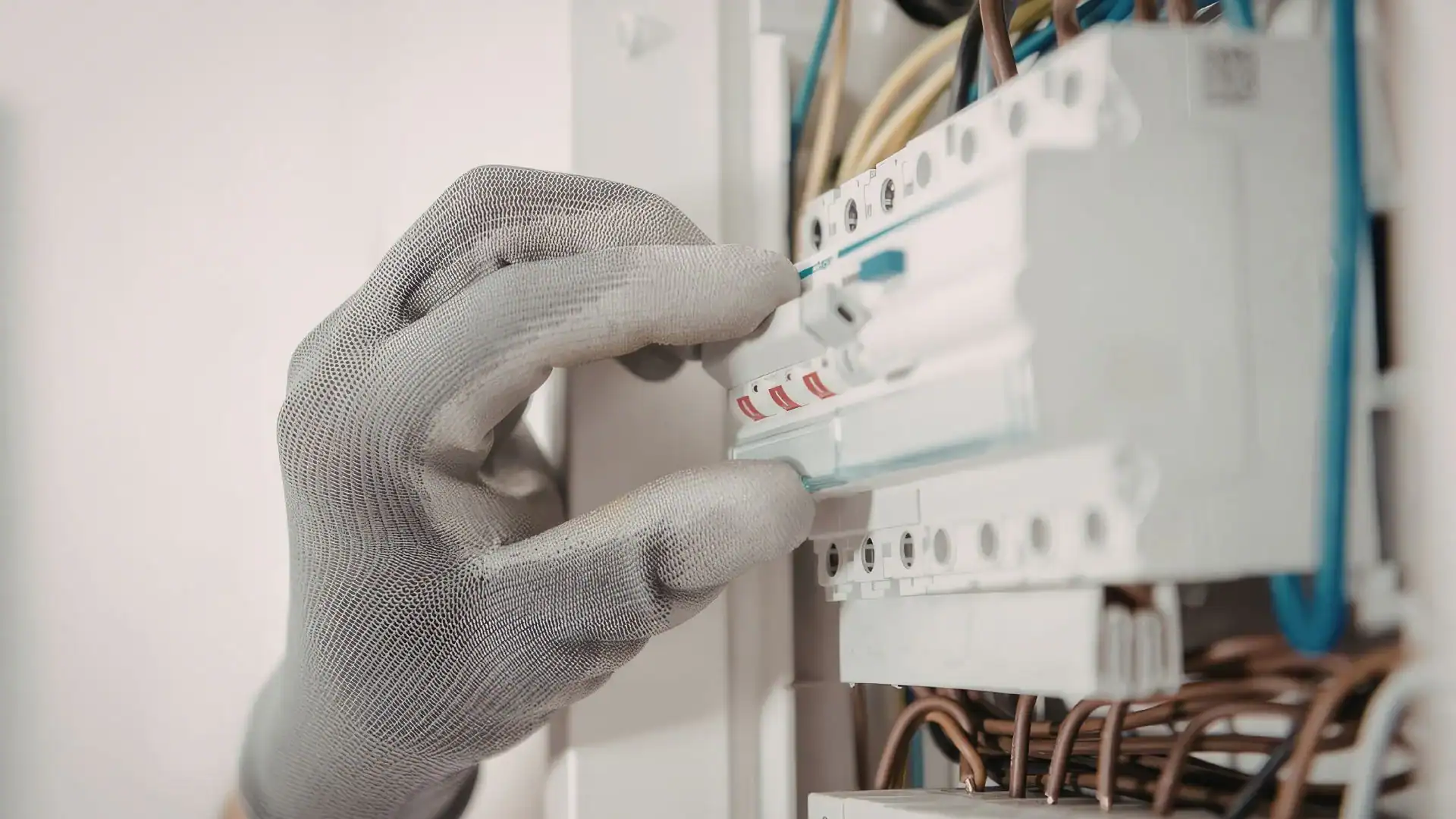 A gloved hand is adjusting a switch or circuit breaker inside an electrical panel with multiple wires and components visible, showcasing the expertise of a pre-eminent electrical service company in Alamance County, NC.