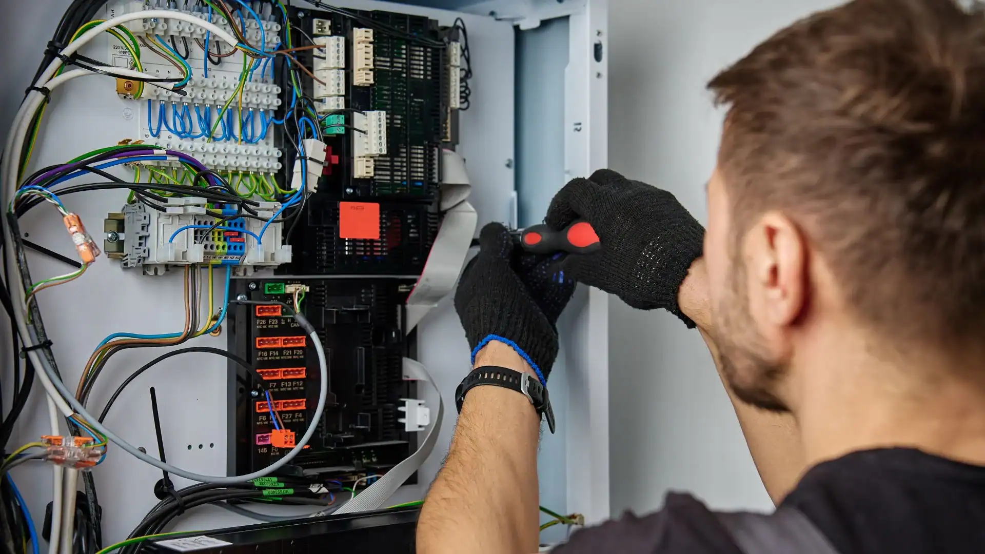 A person wearing black gloves uses a screwdriver to work on wiring inside an open electrical control panel, showcasing the expertise found at Alamance County’s pre-eminent electrical service company in NC.
