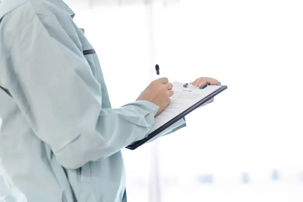 Person in a light blue jacket holding and writing on a clipboard with a pen, standing against a bright, blurred background. The focus is on the hands and clipboard, highlighting an expert from NC's pre-eminent electrical service company in Alamance County.