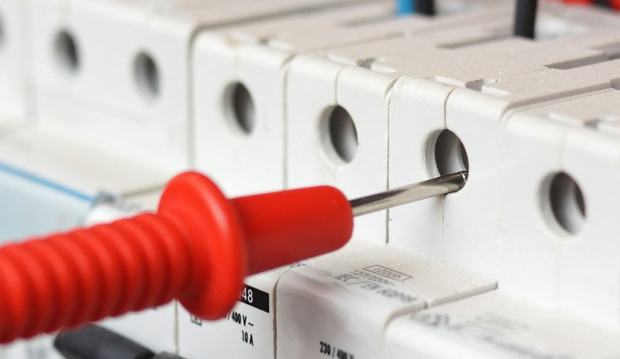 A close-up of a red electrical tester probe inserted into a fuse box or circuit breaker panel, checking the equipment for safety or voltage&mdash;a daily task for a pre-eminent electrical service company in Alamance County, NC.