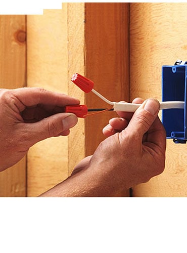 A person twists orange wire connectors onto electrical wires from a blue wall box, preparing wiring inside a wooden wall frame&mdash;a task expertly handled by a pre-eminent electrical service company in Alamance County, NC.